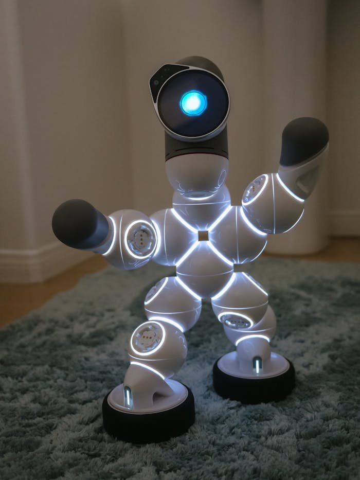 A modern humanoid robot with glowing LED lights, posing on a carpet indoors.